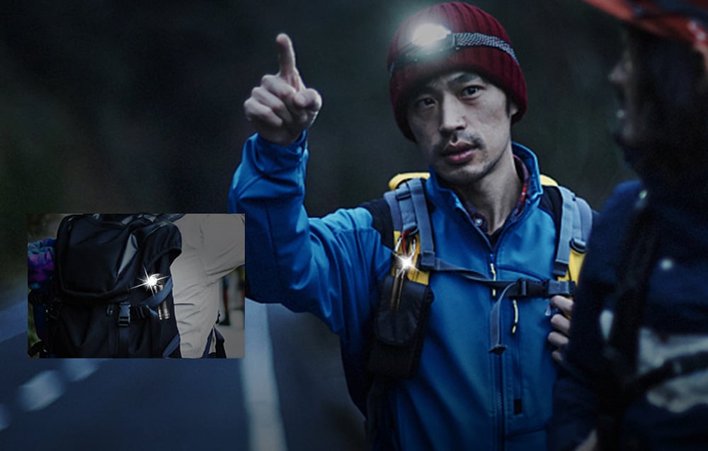 Un homme en veste bleue pointant vers l'avant. Il porte une casquette rouge et une lampe frontale Superfire TH04.