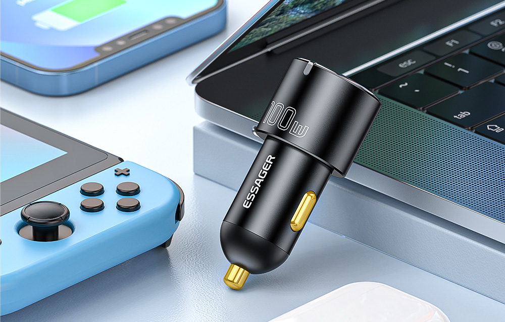 chargeur de voiture noir posé contre un ordinateur portable gris, à côté d'un smartphone et une console de jeux