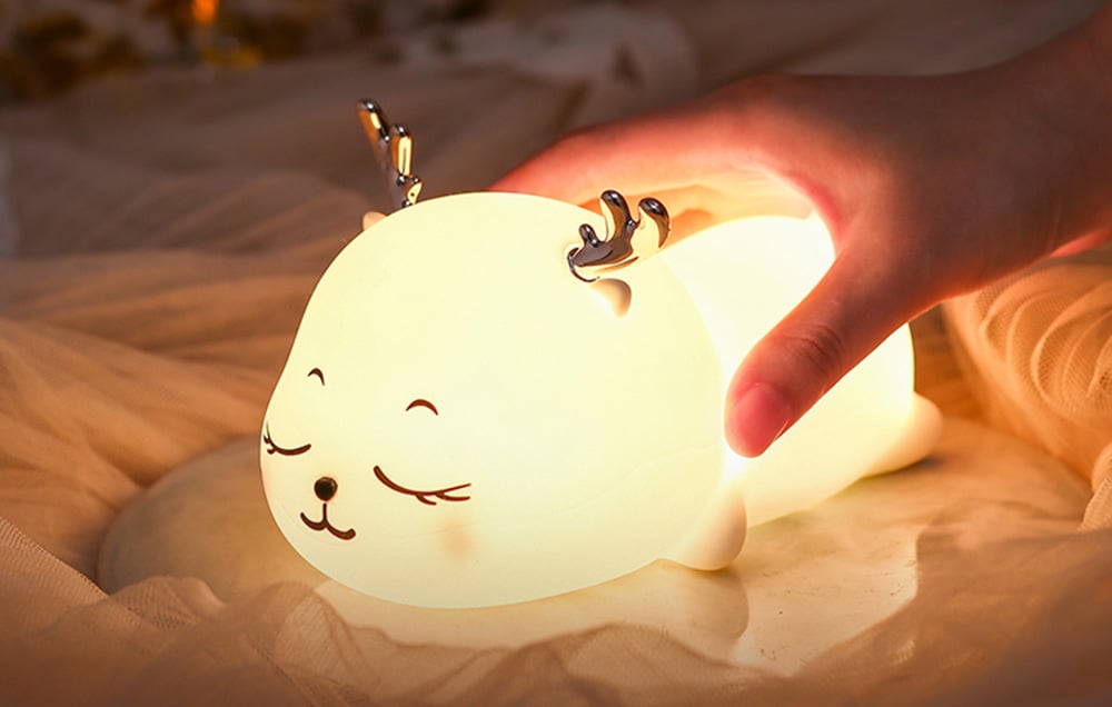 Veilleuse pour enfants : SuperFire L07 Petite Élan émettant une lumière jaune. Une main est visible touchant l'appareil pour ajuster la couleur de la lumière.