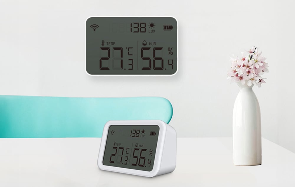 Capteur de température et d'humidité NEO NAS-TH02W avec affichage Zigbee TUYA monté sur un mur, et un autre posé sur une table. À côté, une fleur dans un vase blanc.