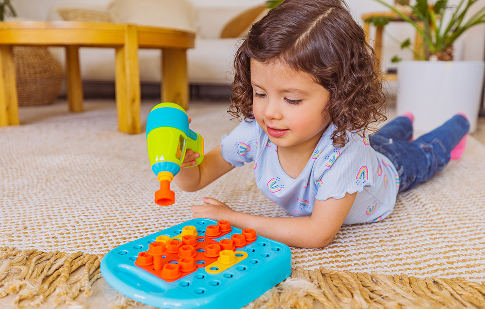 Un enfant allongé sur le tapis visse des vis dans le tableau à l'aide de la perceuse Learning Resources EI-4107.