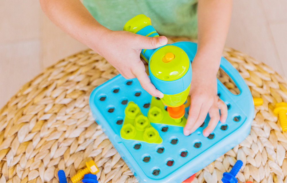 Un enfant visse une tuile dans le plateau à l'aide de la perceuse Learning Resources EI-4107.
