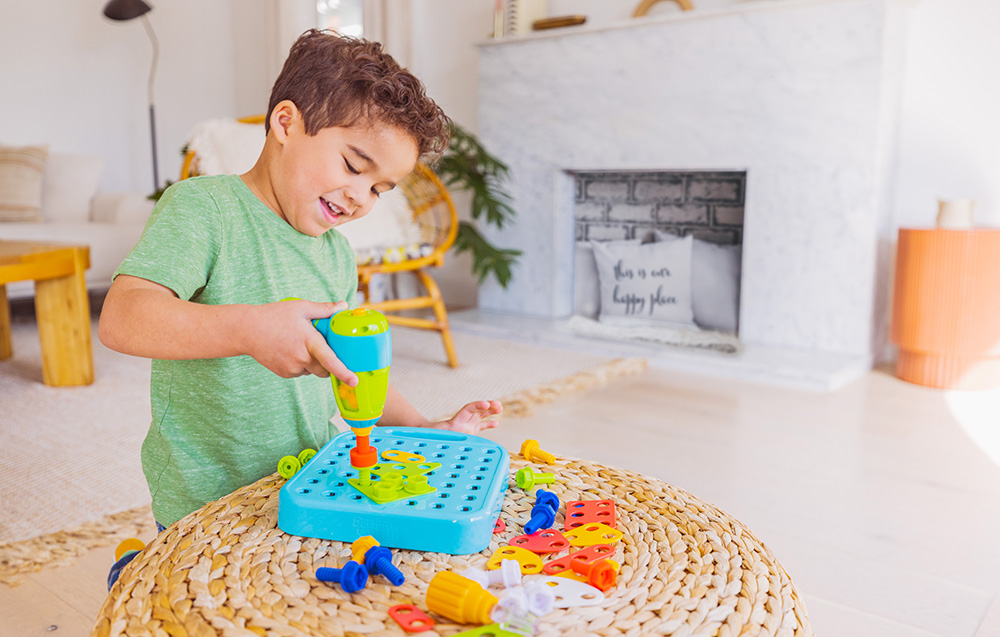 Un enfant vissé des tuiles dans le plateau à l'aide de la perceuse Learning Resources EI-4107. Une cheminée est visible en arrière-plan.