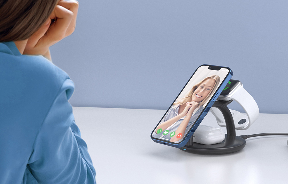 une femme passe un appel vidéo sur un téléphone connecté avec des écouteurs et une montre connectée au chargeur inductif